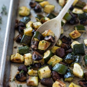 Roasted zucchini and mushrooms on a sheet pan with a wooden spoon