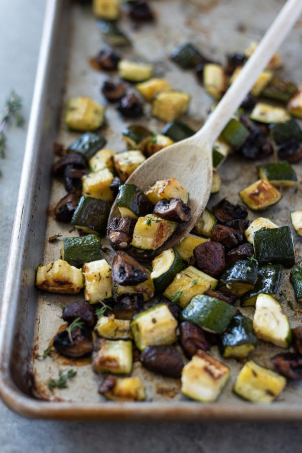 Roasted zucchini and mushrooms on a sheet pan with a wooden spoon