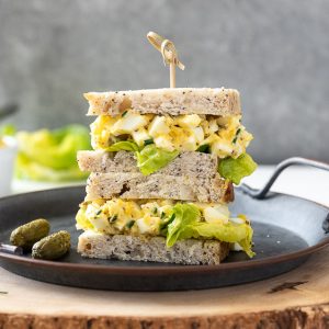 egg salad sandwich piled on a plate with a wooden pick