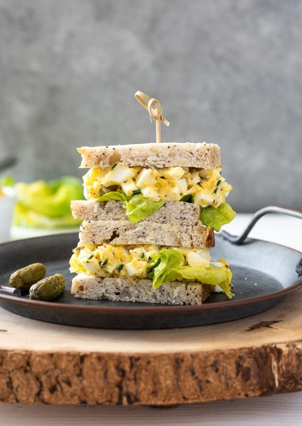 egg salad sandwich piled on a plate with a wooden pick