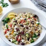 greek orzo salad in a white bowl with spoon buried into the side