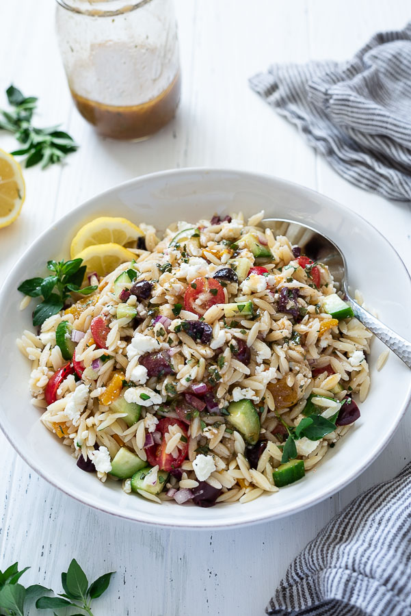 greek orzo pasta salad in a white bowl with spoon buried into the side