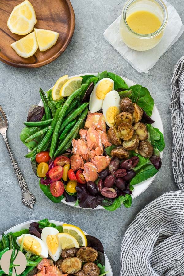 Salmon nicoise salad on white plate with fork and linen alongside