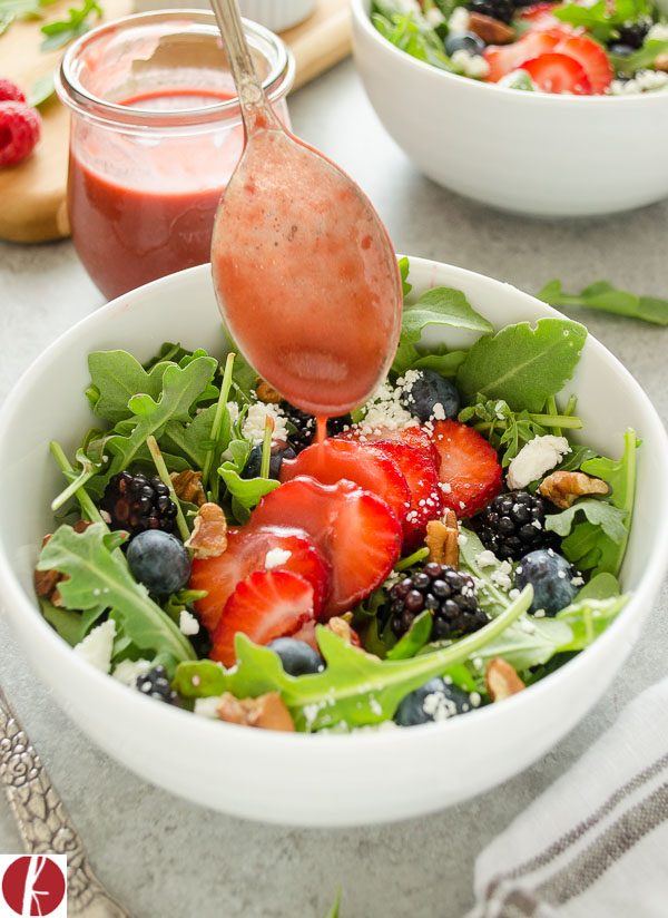 Close up of raspberry balsamic dressing drizzling over arugula salad
