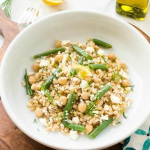 Pearl barley salad in white bowl with green beans and lemon