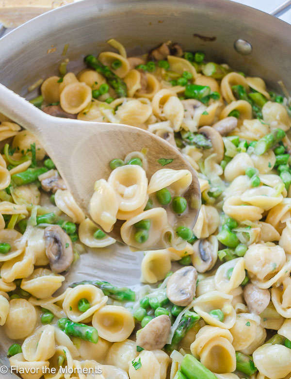 creamy pasta primavera being scooped up by a wooden spoon