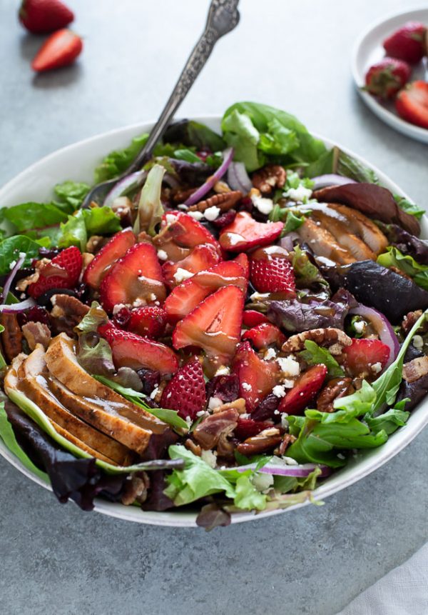 close up of strawberry fields salad with balsamic dressing on top and spoon buried inside bowl