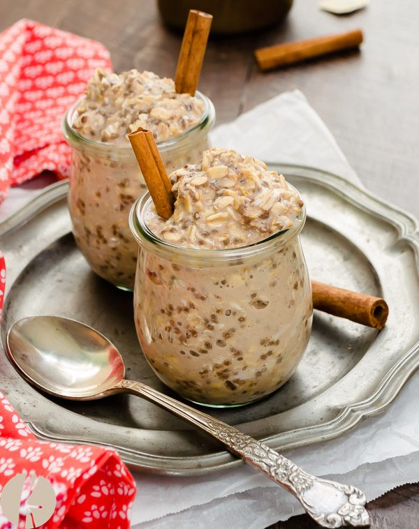 front view of overnight oats in jars on a plate with spoon and cinnamon stick