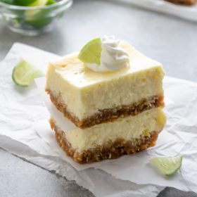 Key lime cheesecake bars on parchment with whipped cream and lime
