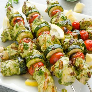 pesto chicken skewers piled on a white plate