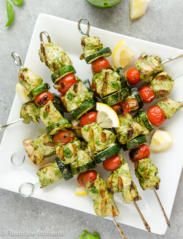 overhead shot of grilled pesto kebabs on a white plate with lemon slices