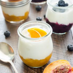 fruit on the bottom yogurt in jar with spoon and fresh peach on top