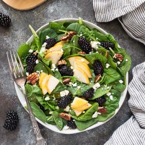 Power green salad with pears and blackberries on a white plate