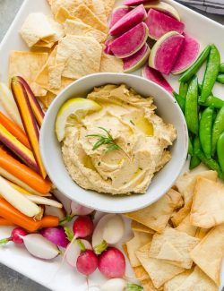 Lemon hummus in bowl surrounded by vegetables