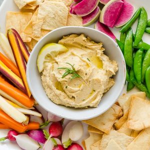 Lemon hummus in bowl surrounded by vegetables