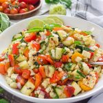 Zucchini and corn salad in white bowl with basil and lime on top