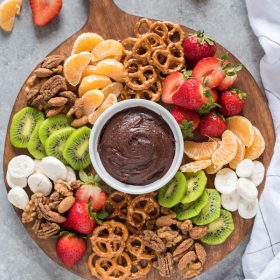 Party platter on wooden cutting board with chocolate hummus, fruit and nuts