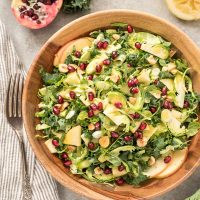 Kale Brussels Sprout Salad in teak bowl with pomegranates on top