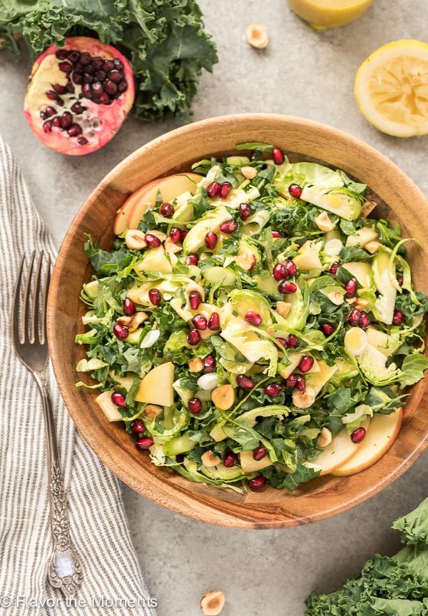 Kale Brussels Sprout Salad in teak bowl with pomegranates on top