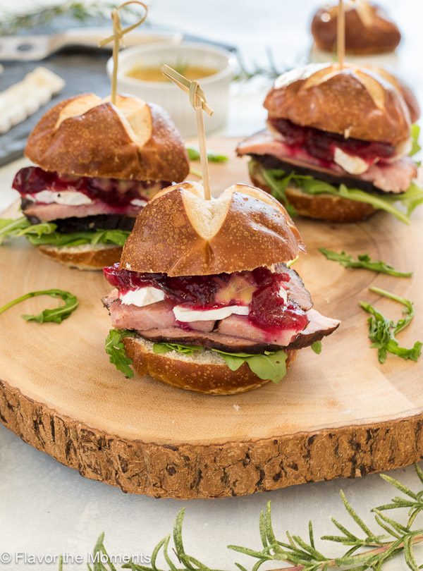 Ham sliders on a serving plate with brie, arugula and cranberry sauce
