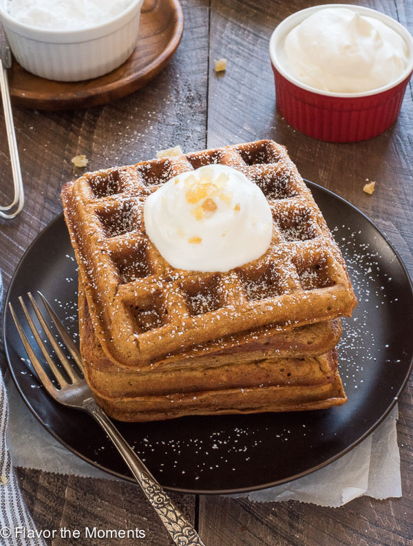 Stack of gingerbread waffles with whipped cream and candied ginger on top