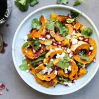 Roasted delicata squash with pomegranate and goat cheese on white plate