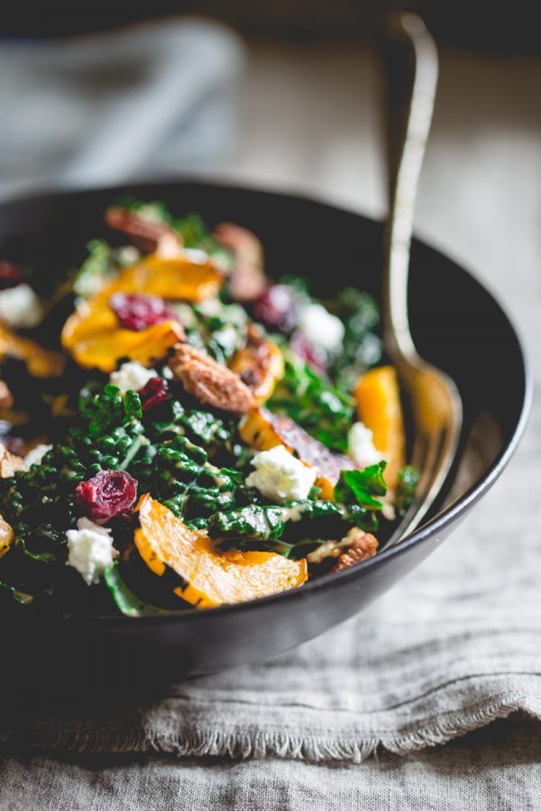 Kale salad with roasted delicata squash in a bowl with spoon