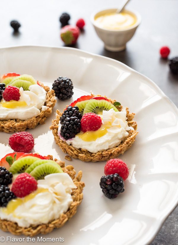 Close up of breakfast fruit tarts on white platter with fruit and lemon curd