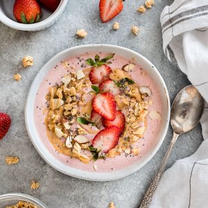 Strawberry smoothie bowl in white bowl with granola and fruit on top