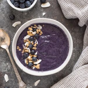 Blueberry banana smoothie bowl in white bowl with granola and berries on top