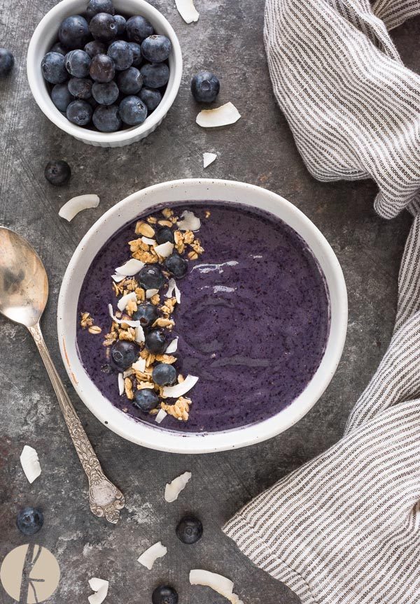 blueberry banana smoothie bowl in white bowl with granola and berries on top
