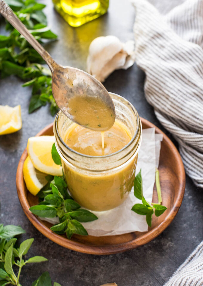 Spoon drizzling Greek salad dressing into a jar.