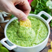 Avocado salsa verde dip in white bowl with chip dipped in