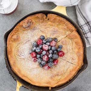 dutch baby pancake in skillet with berries and powdered sugar
