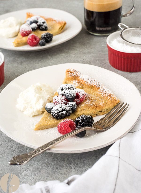 slice of dutch baby pancake on a plate with berries and whipped cream