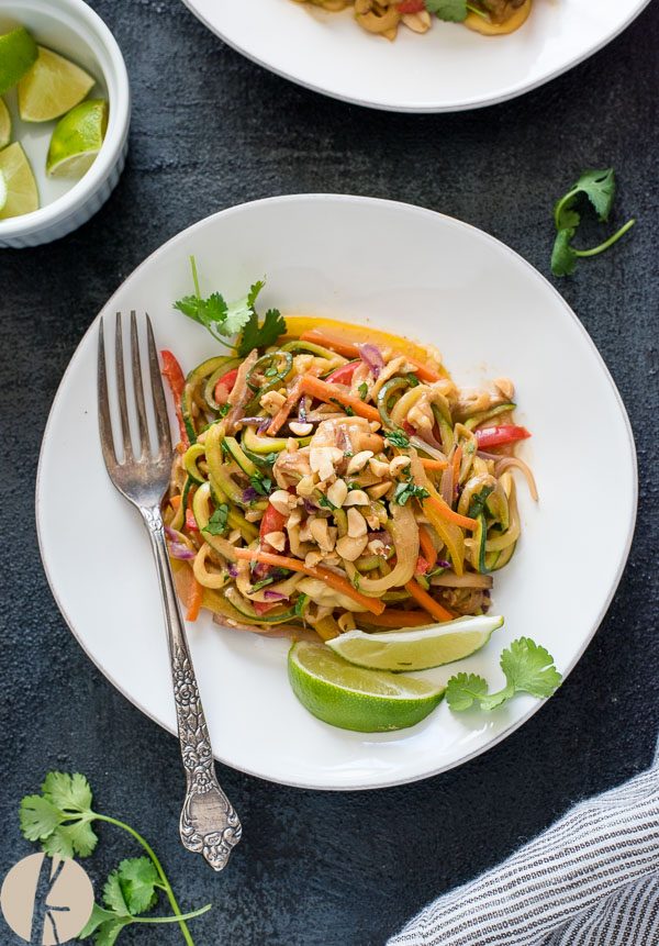 Vegetarian thai peanut zucchini noodles on a white plate with fork and lime