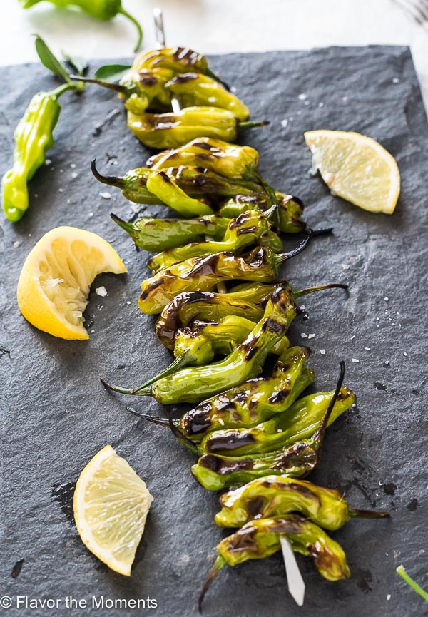 Grilled shishito peppers on serving board with lemon and sea salt