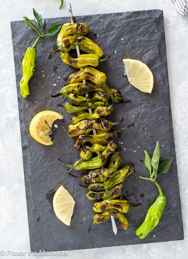overhead shot of Grilled Shishito Peppers on a serving platter with lemon