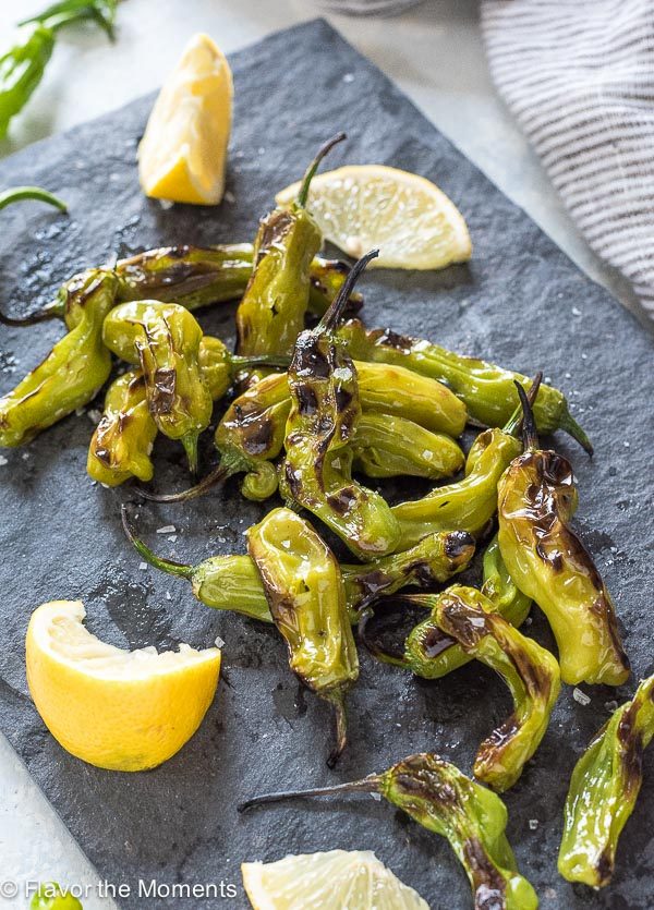 Grilled Shishito Peppers piled on a serving platter with lemon
