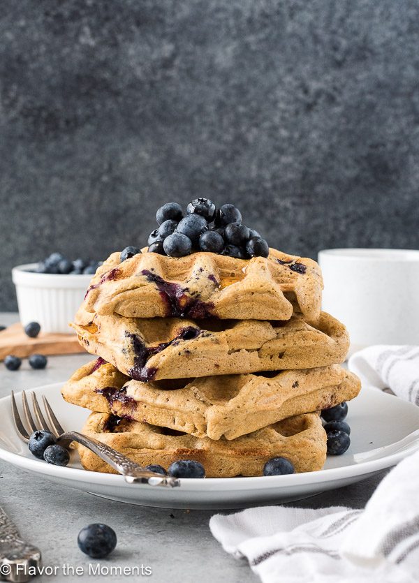 Stack of oat flour waffles on a plate with blueberries on top