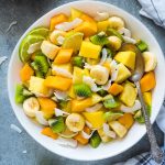 Tropical fruit salad in a white bowl with coconut flakes