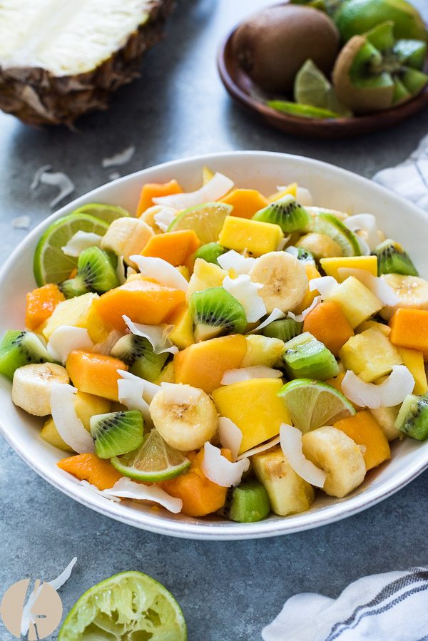 Tropical fruit salad in a white bowl with coconut flakes 
