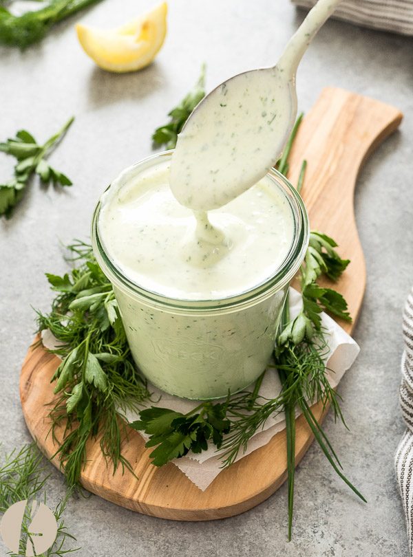 Greek yogurt ranch drizzling off of spoon into a jar