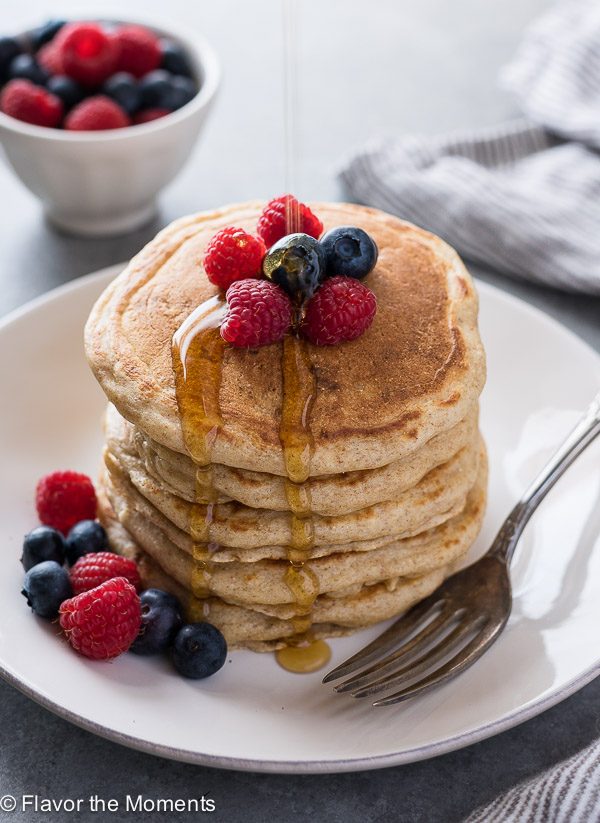Stack of Greek yogurt pancakes on a plate with berries on top and maple syrup dripping down