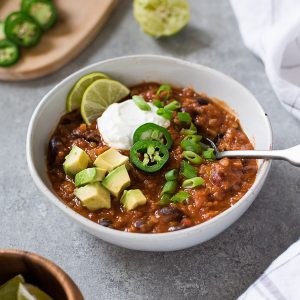Bowl of taco lentil chili with avocado and scallions on top