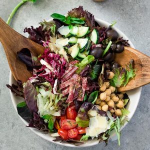 Italian chopped salad in white bowl with wooden servers