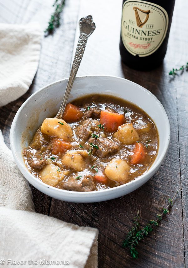 Bowl of Irish beef stew with spoon buried inside and Guinness behind