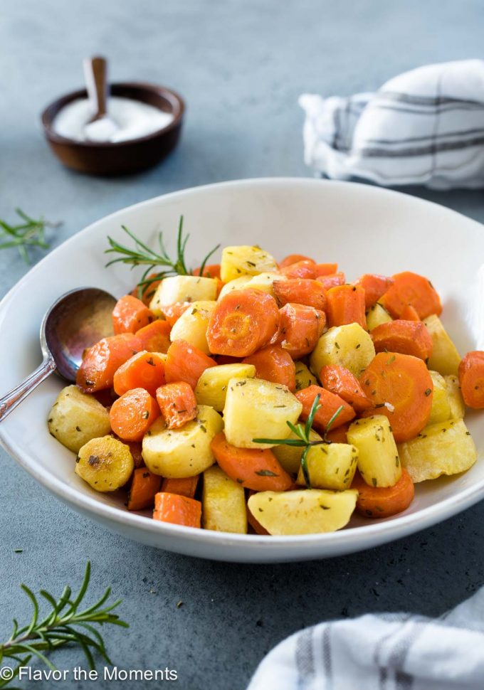 Roasted carrots and parsnips in a white bowl with spoon