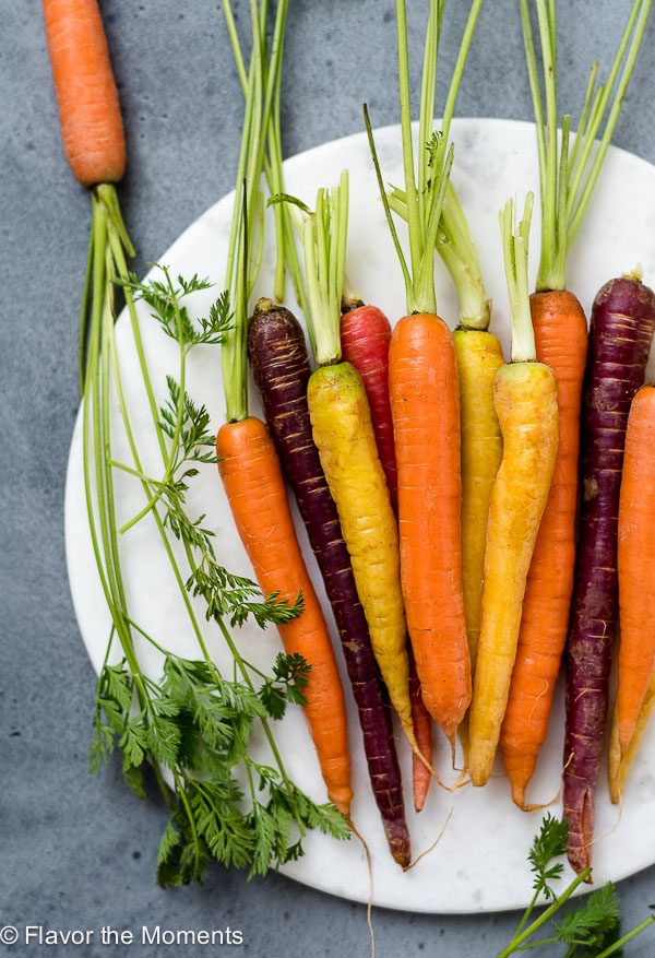 Rainbow carrots with carrot tops on a white marble board