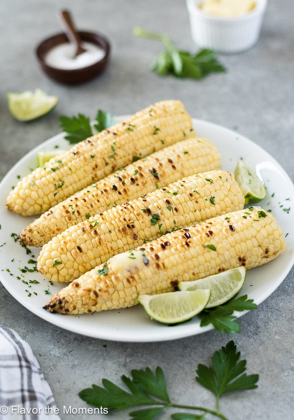 grilled corn on the cob on a white plate with lime wedges and melted butter